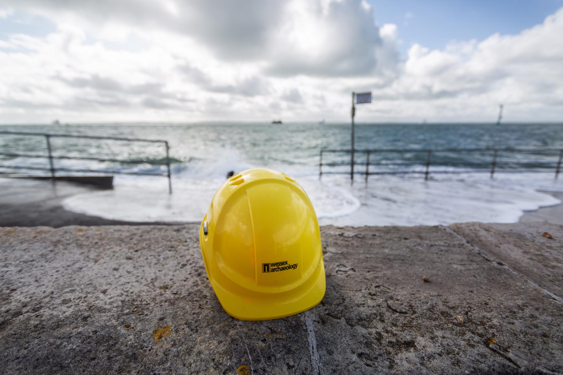 A builder's hat with the Wessex Archaeology logo is shown in front of the incoming tide.