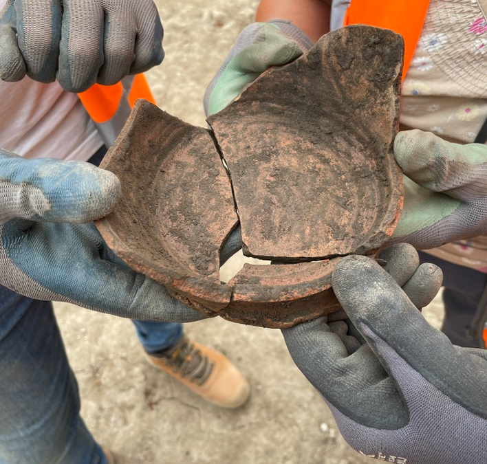 Three people hold three sherds of pottery together to form the base of a bowl.