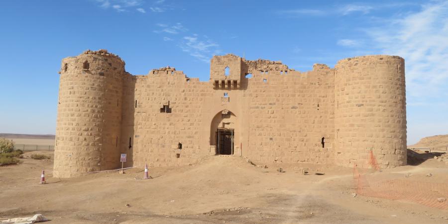 Al-Muazzam Fort made from reddish yellow carved stone. The arched entrance is flanked by curved tower on each side. 