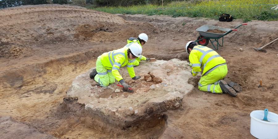 A group of 3 field archaeologists excavate the remains of a medieval kiln near Sizewell.