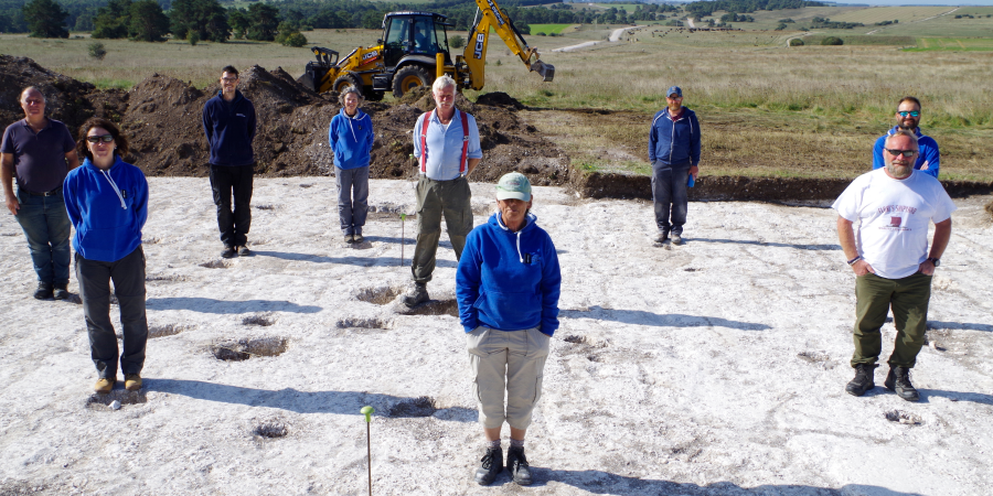 The team stand on site around postholes of a roundhouse revealed in 2020