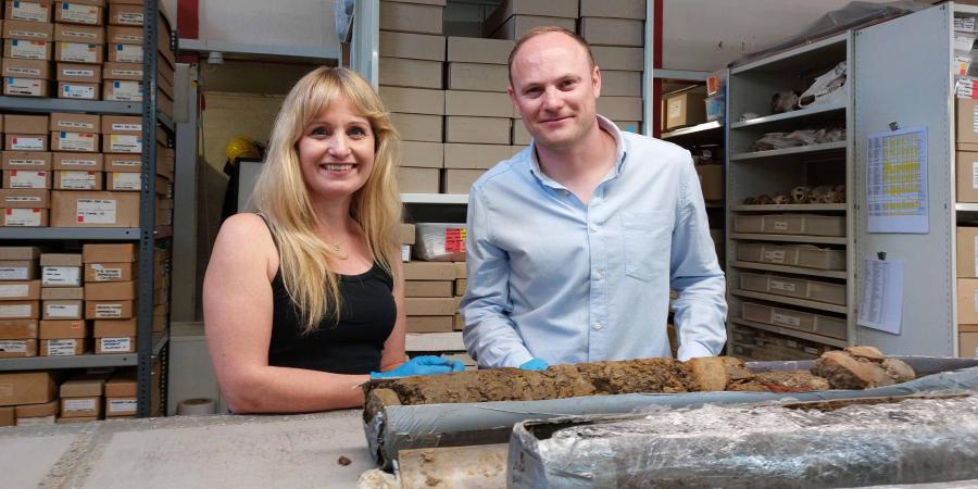 Dr Cat Jarman and Dr Daniel Young are looking at the camera. In front of them on a desk is a sample from Sheffield Castle