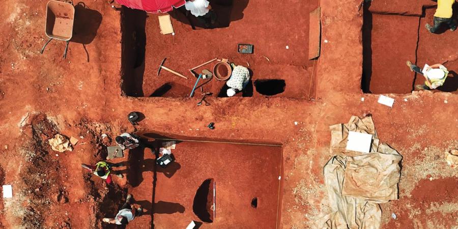 Excavation for the MOWAA Archaeology Project: looking down on the deep red earth, archaeologists excavate and half section pits