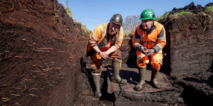 Archaeologists Max Dampier and Arthur Hollindrake are stood in a deep trench, inspecting the layers of peat.