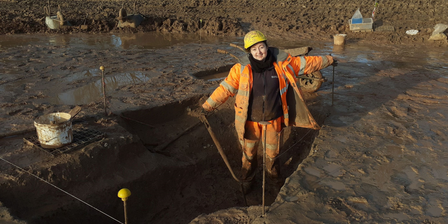 Archaeologist wearing PPE stands in trench