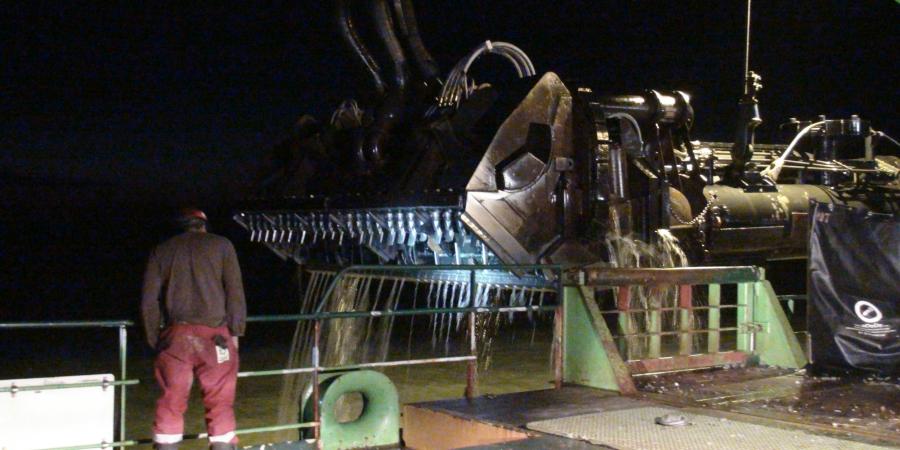 An aggregate hopper oozes sea water. The night is pitch black and a lone man stands on deck