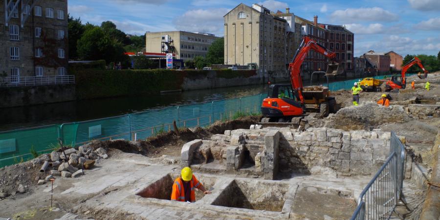 Archaeological excavation underway with historic building behind