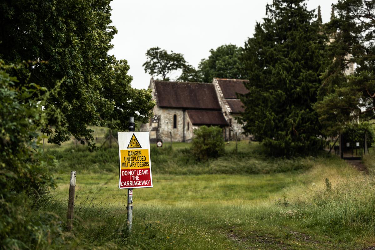 Military sign warning of unexploded debris sits in front of an abandoned church enclosed by old trees