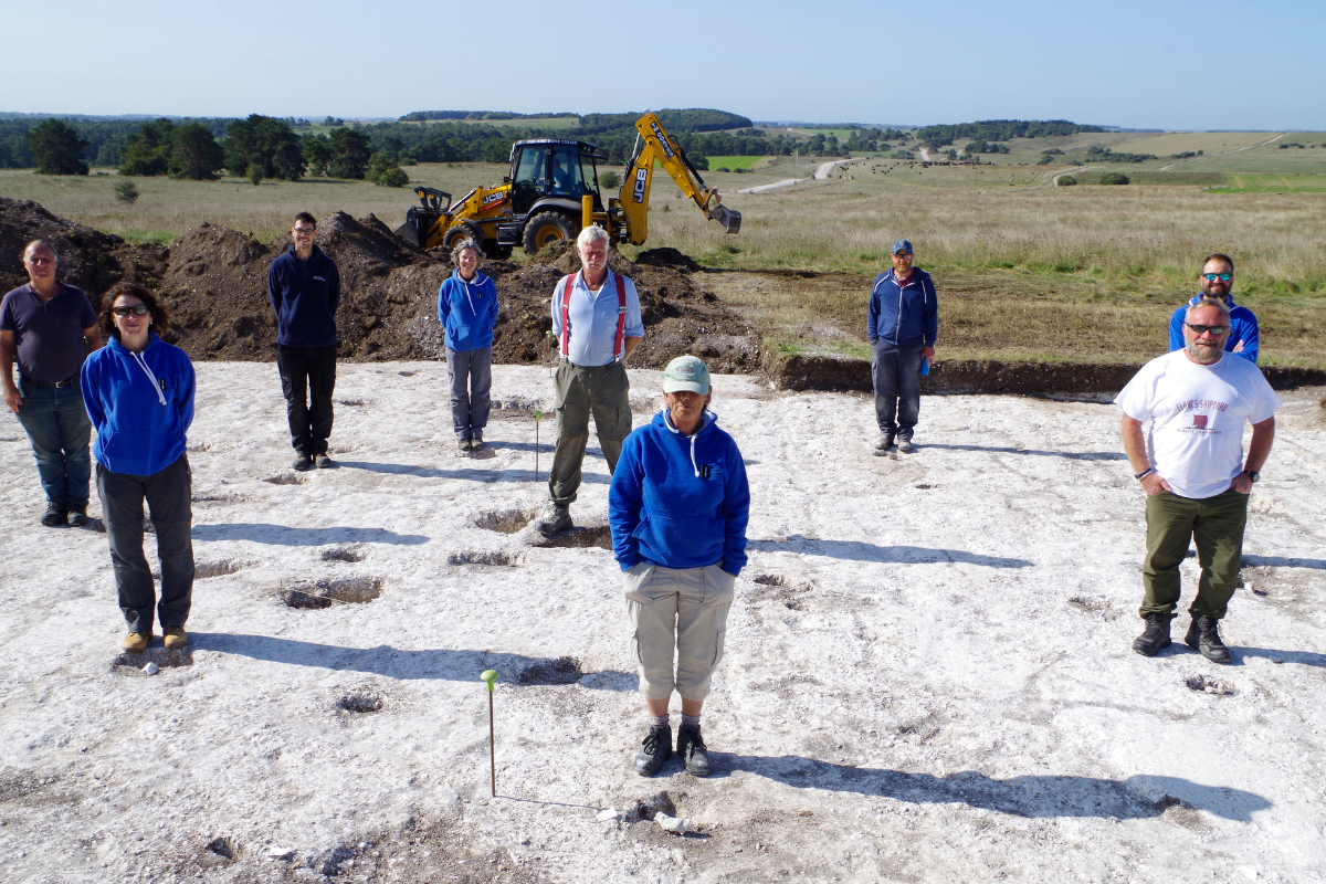 The team stand on site around postholes of a roundhouse revealed in 2020