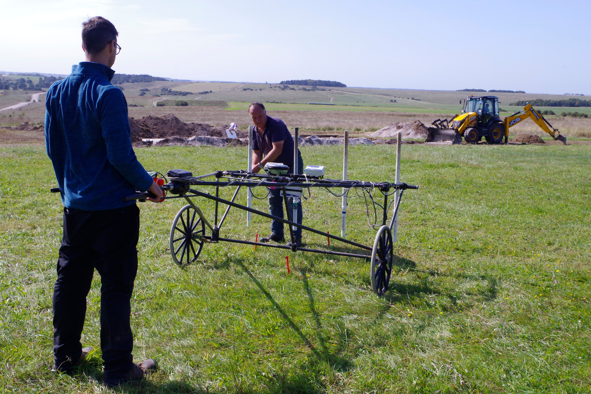 Two people stand next to equipment used in extensive geophysical survey of the surrounding area