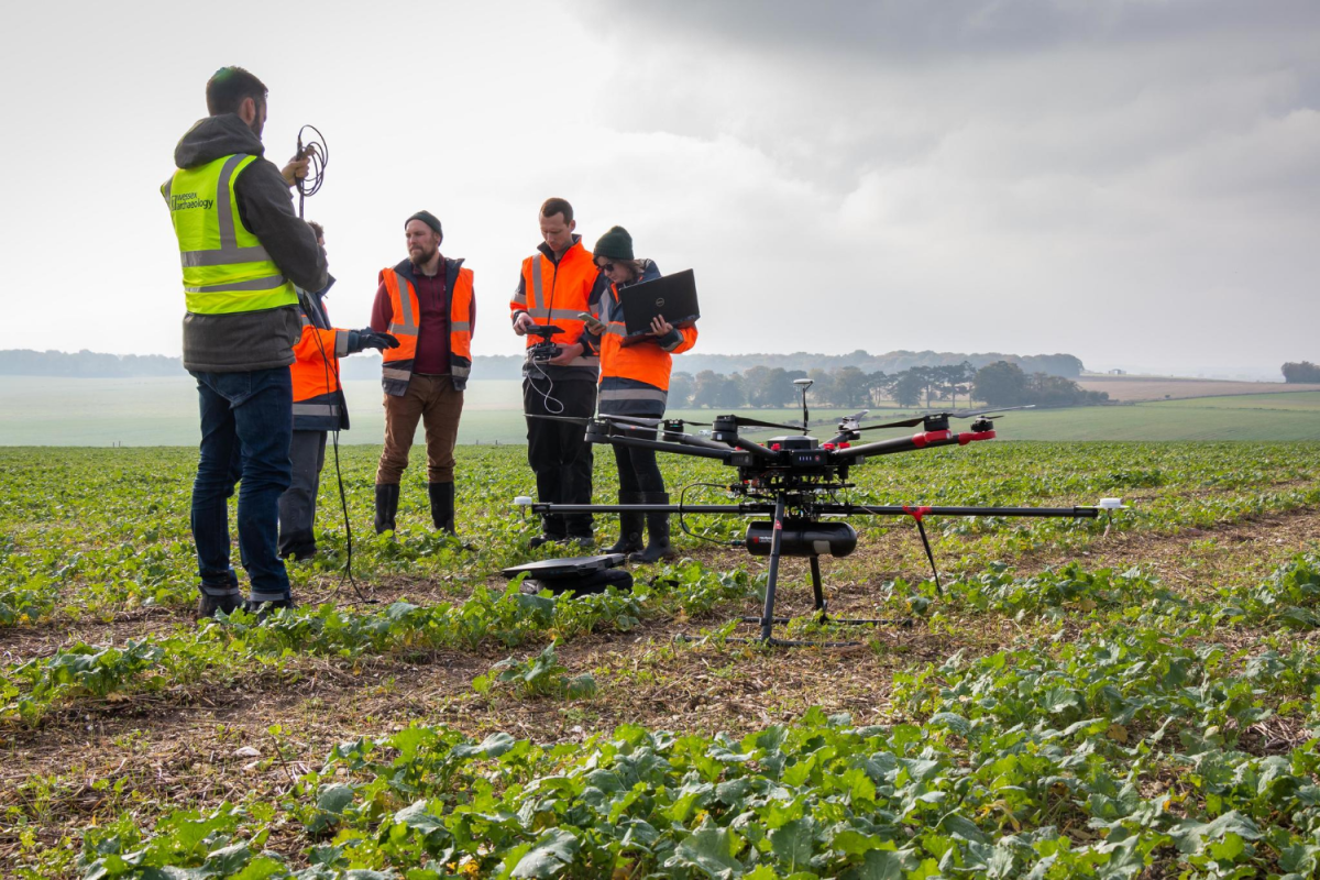 Group stands in landscape with drone on ground before them - 'capturing ROV footage'