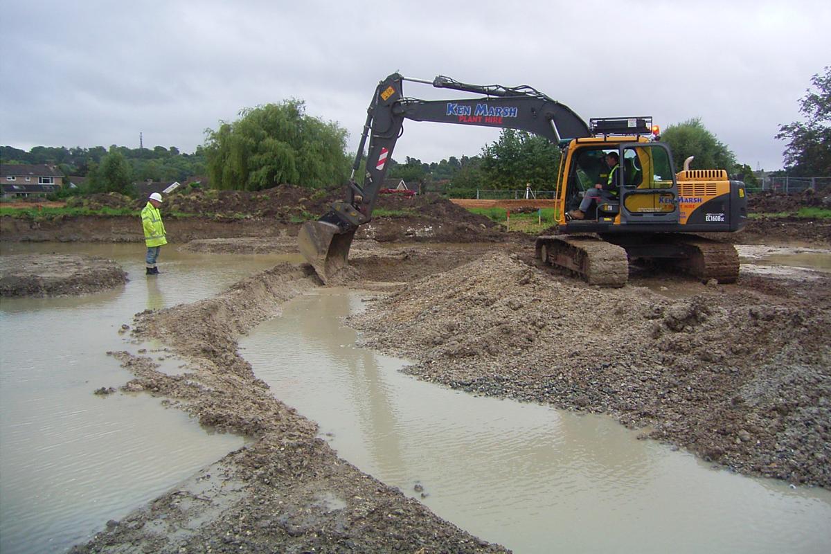Wet conditions during excavation: an archaeologist stands above a trench filled with water