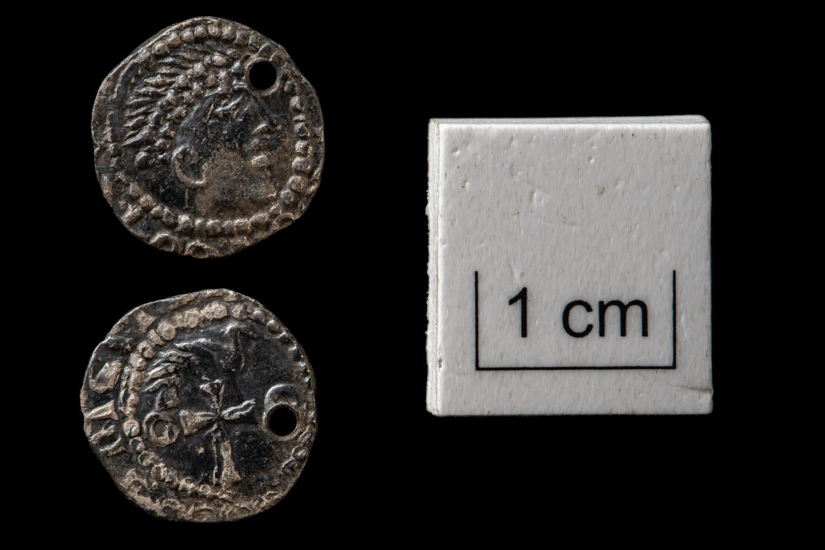Head and tails of two small, pierced, silver coins on a black background