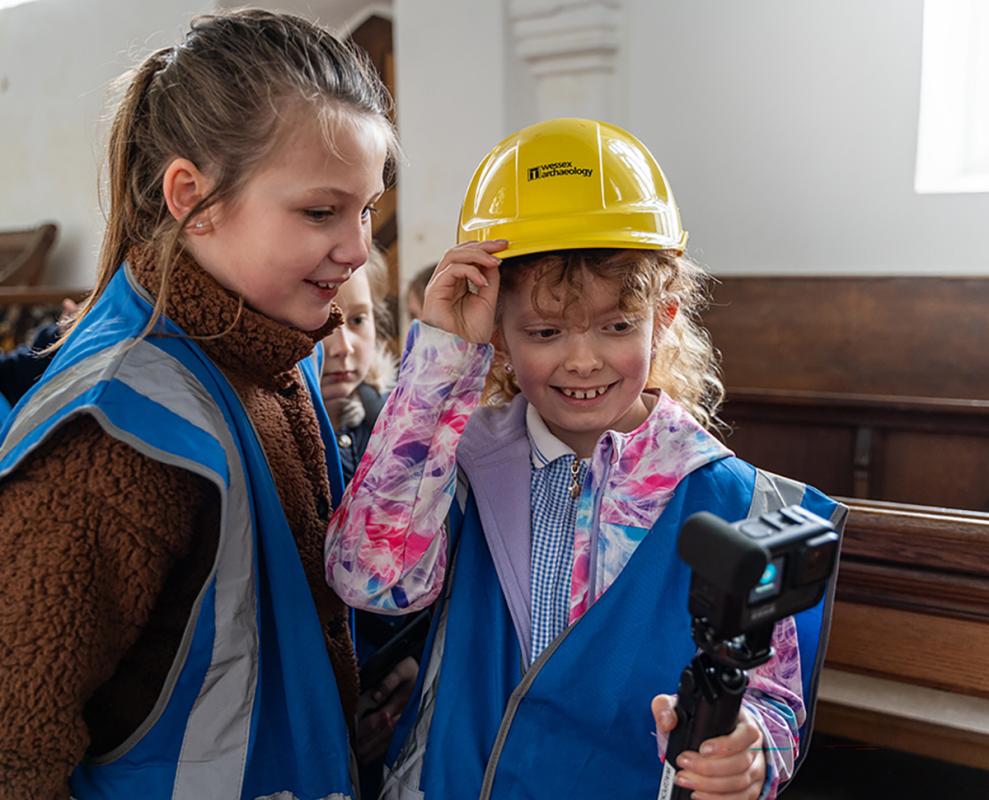 school children in high visibility jackets hold camera in church 