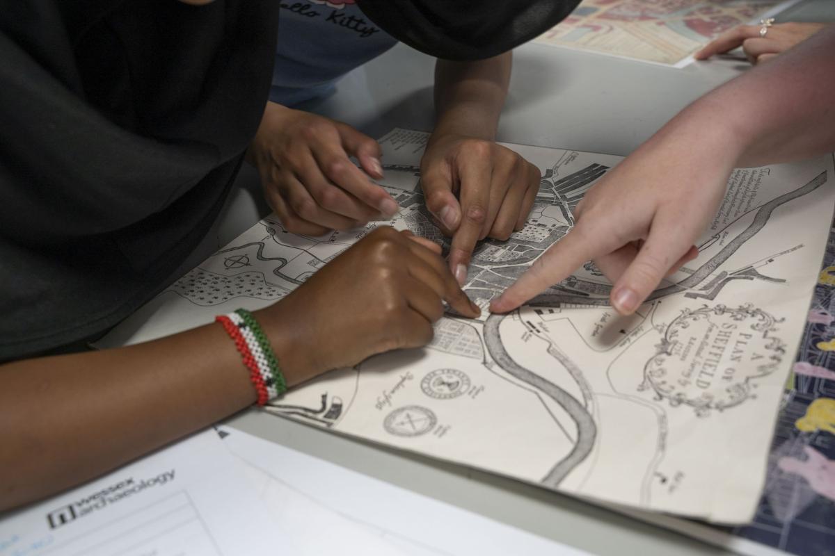 Four hands belonging to four pupils point to an old map. A big meandering river and 18th century housing can be seen. The pupils point to the location of Sheffield Castle 
