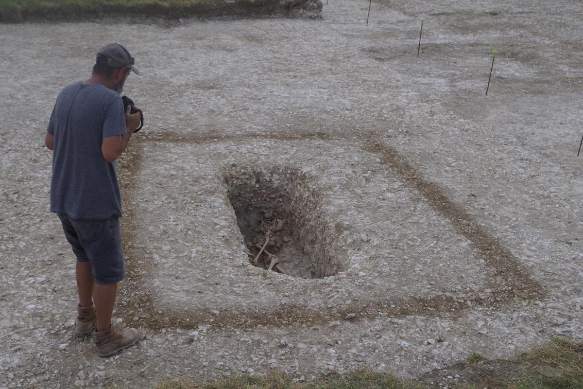 An excavated grave cut into the chalk bedrock in enclosed by square shadow of degraded timber