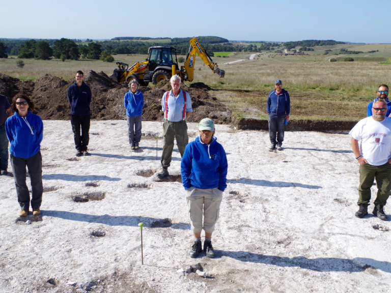 The team stand on site around postholes of a roundhouse revealed in 2020