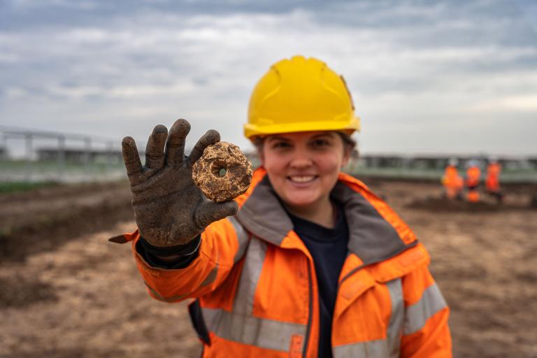 Archaeologist on site in full protective equipment holding an artefact