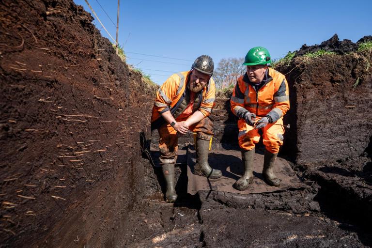 Archaeologists Max Dampier and Arthur Hollindrake are stood in a deep trench, inspecting the layers of peat.