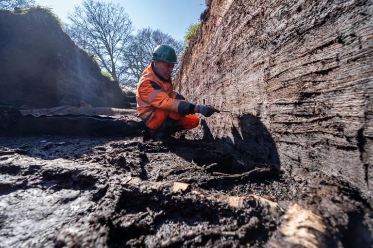 Archaeologist Arthur Hollindrake is crouched next to the trackway.
