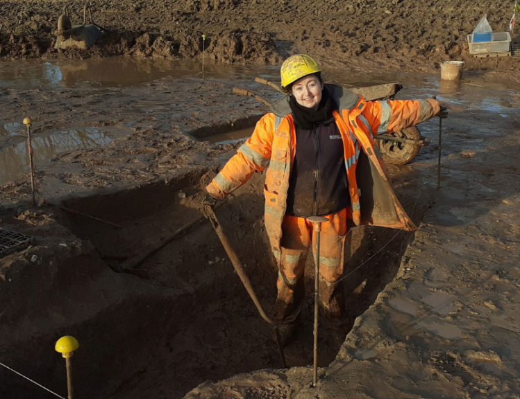 Archaeologist wearing PPE stands in trench