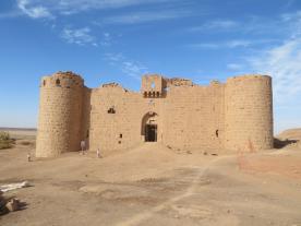 Al-Muazzam Fort made from reddish yellow carved stone. The arched entrance is flanked by curved tower on each side. 