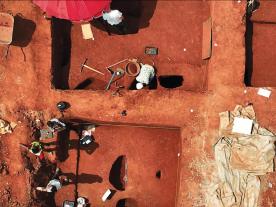 Excavation for the MOWAA Archaeology Project: looking down on the deep red earth, archaeologists excavate and half section pits
