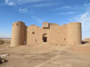 Al-Muazzam Fort made from reddish yellow carved stone. The arched entrance is flanked by curved tower on each side.